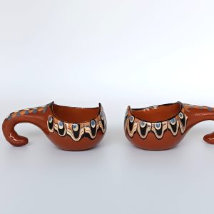 Pair of vintage Bulgarian Troyan pottery miniature ceramic cups with curved handles, traditional Peacock Eye decoration and brown glaze, dating from the 1970s–1980s, side view.