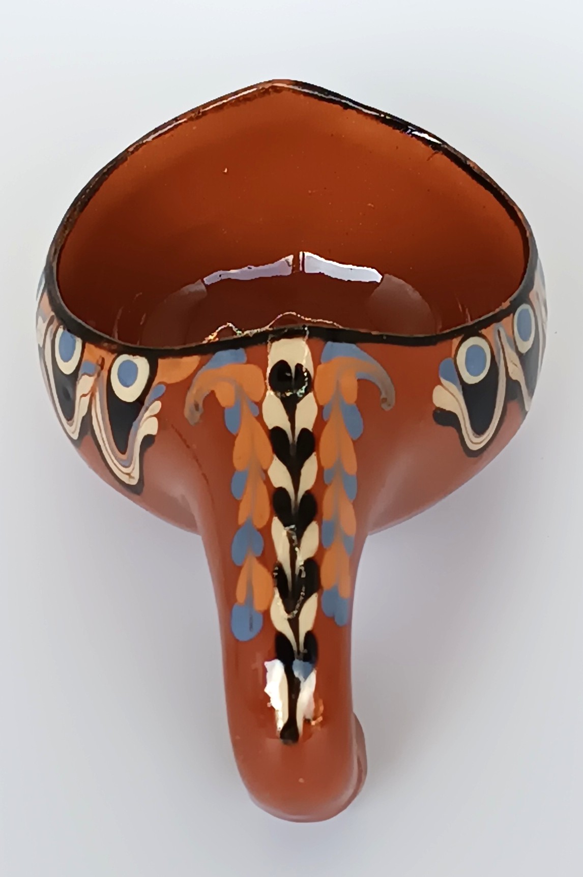 Top view of a vintage Bulgarian Troyan pottery miniature ceramic cup showing its decorated curved handle, glossy brown interior and traditional Peacock Eye pattern in blue, cream and black.