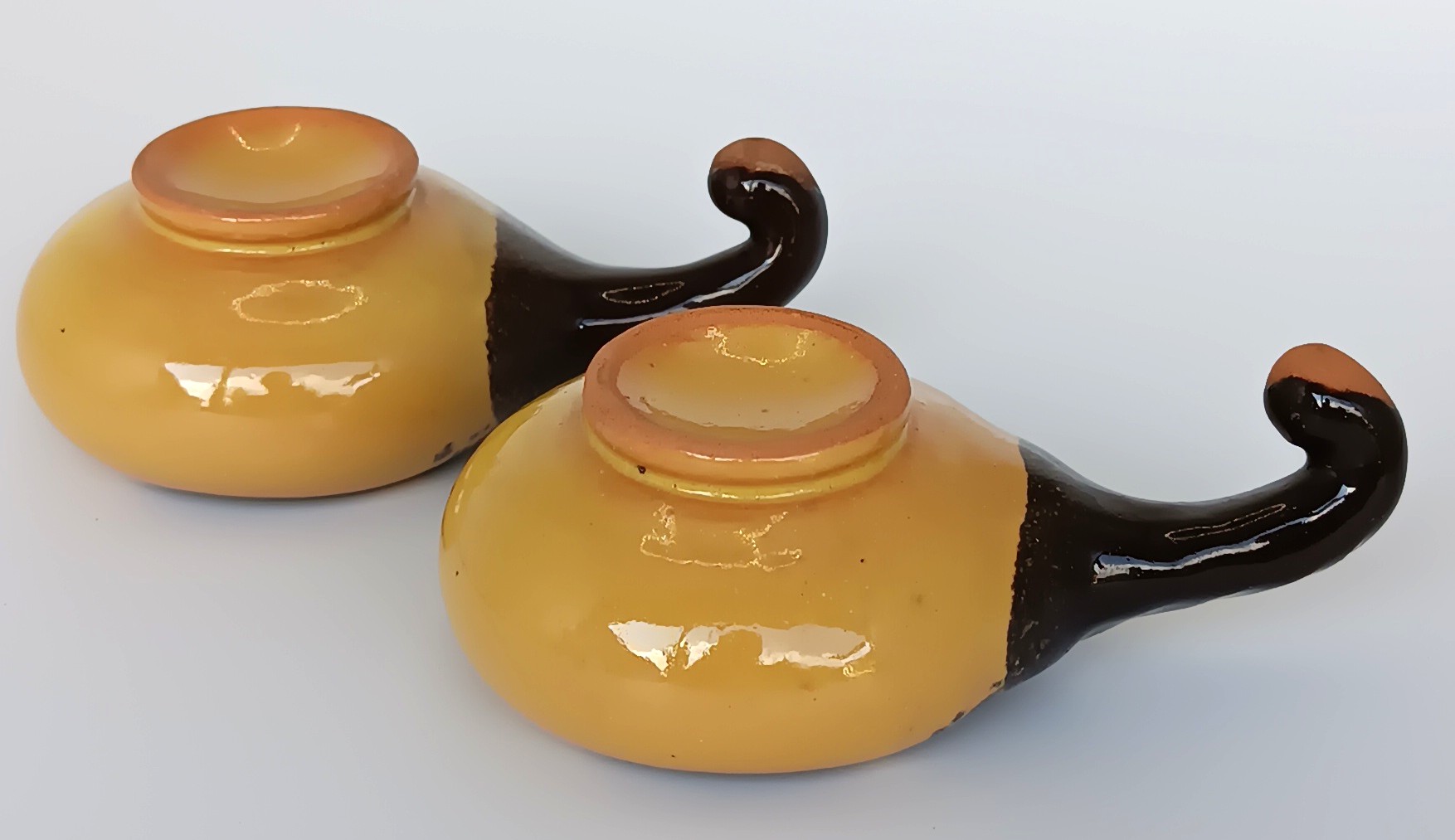 Base and handle view of two vintage ceramic Schnapspfeifle pipe-shaped liqueur cups with ochre yellow glaze and dark brown handles
