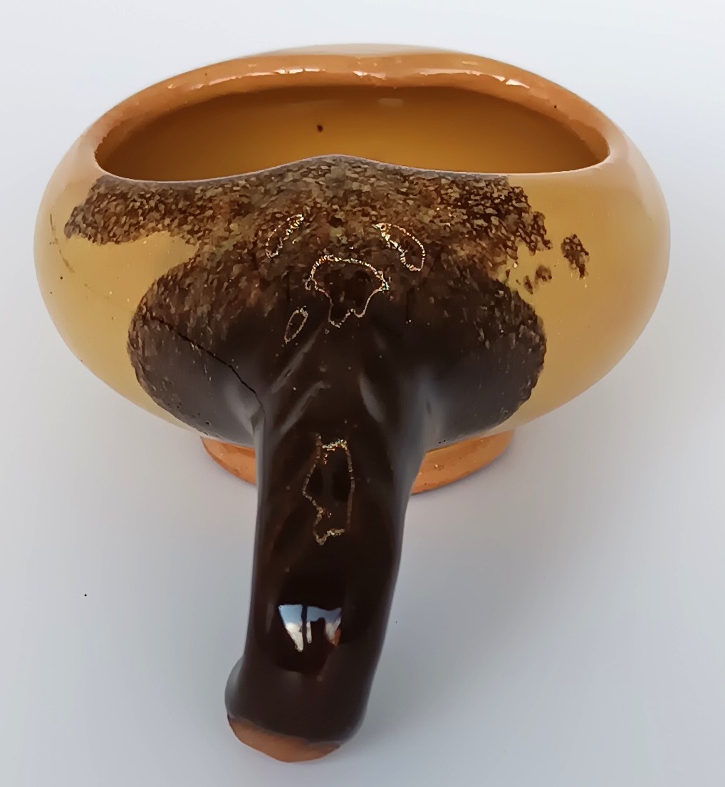 Close-up of a vintage ceramic Schnapspfeifle pipe-shaped liqueur cup showing the dark brown handle and ochre yellow glazed body