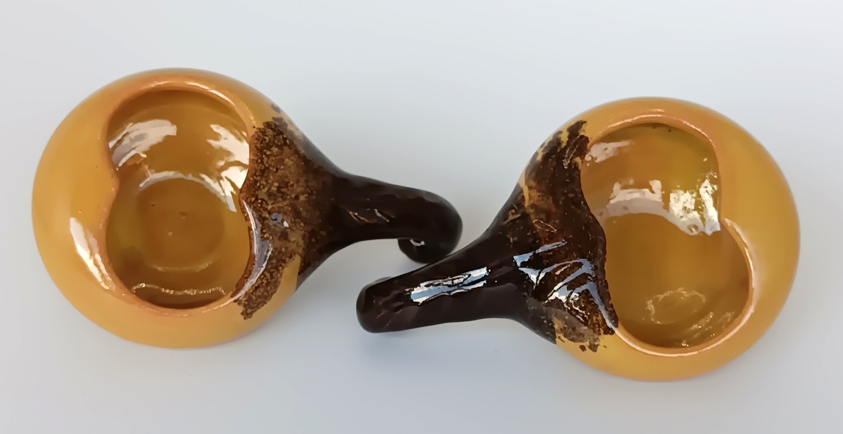 Top view of a pair of vintage ceramic Schnapspfeifle pipe-shaped liqueur cups with ochre yellow glaze and dark brown handles