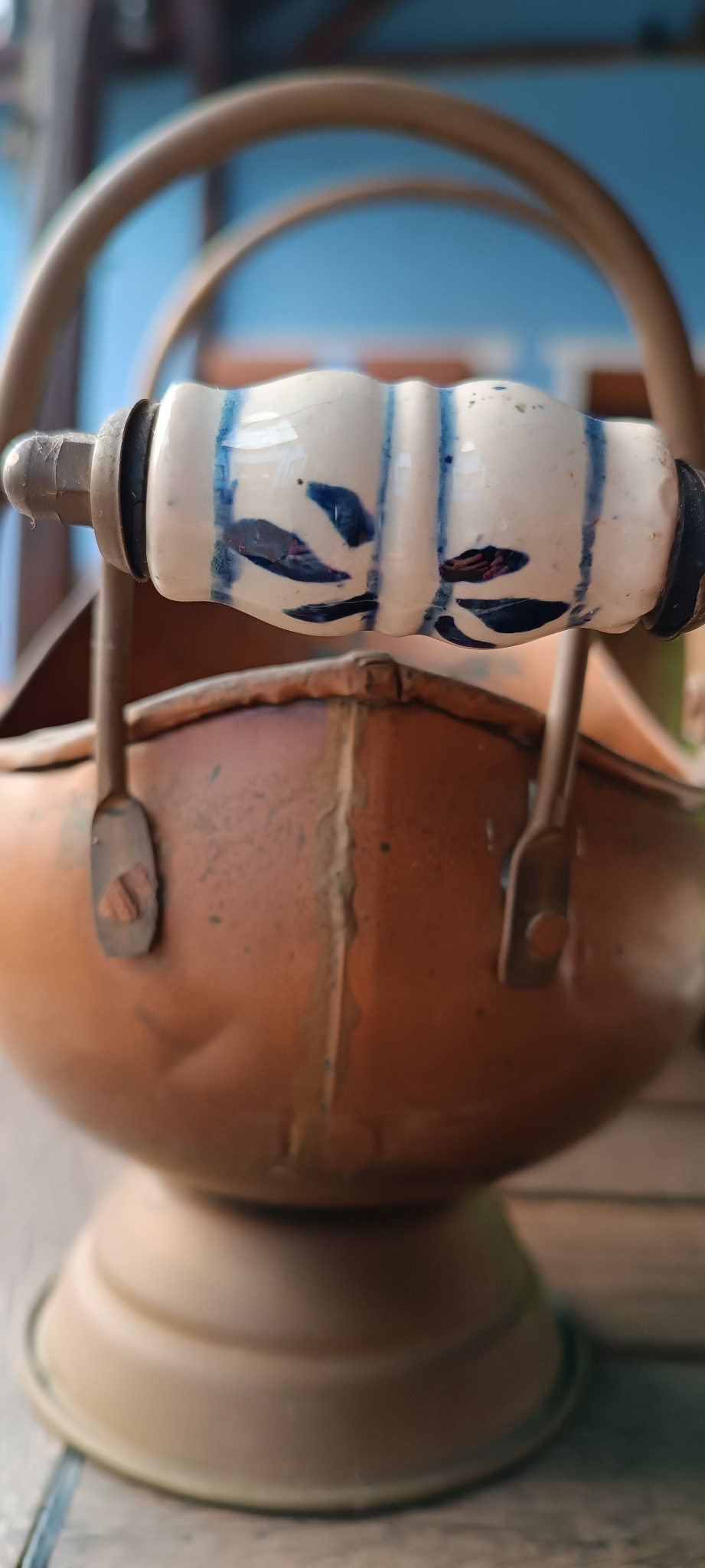 Rear view of blue-and-white ceramic grip on vintage copper scuttle showing metal fittings, attachment points and surrounding seam details