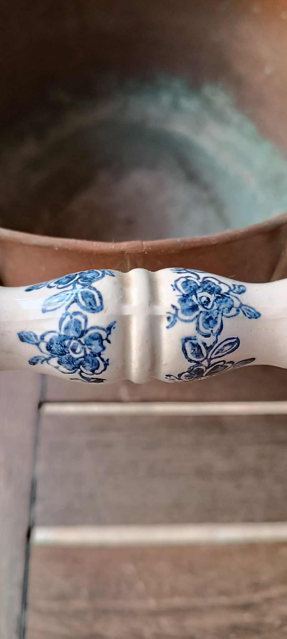 Close-up of blue floral Delft-style motifs on a white ceramic grip fitted to a vintage Dutch copper coal scuttle