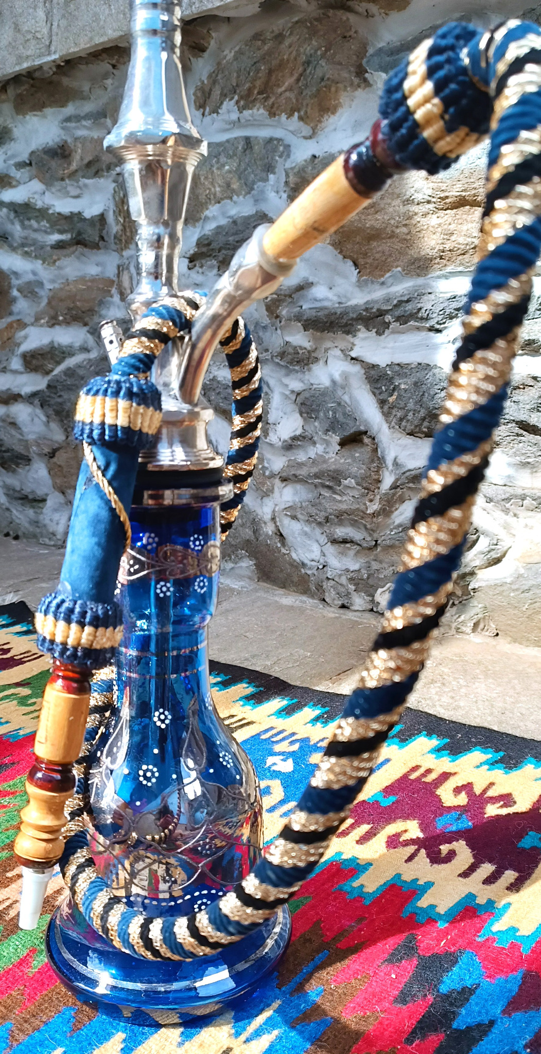 Detail of the polished metal stem and curved hose connector of a vintage Egyptian Yehia El Khawanky hookah with blue-and-gold braided hose and cobalt glass base